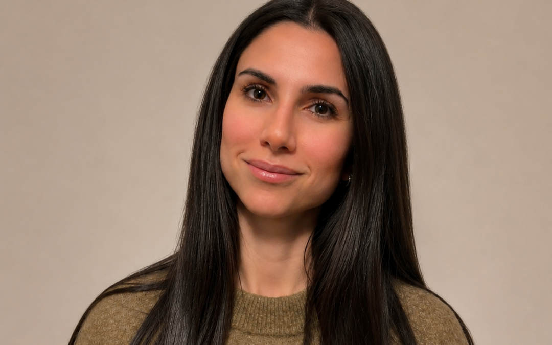 Med et roligt smil ser Sanaz Amin Guldmann ind i kameraet mod en lys baggrund, mens hendes lange, mørke hår og brune striktrøje træder tydeligt frem.